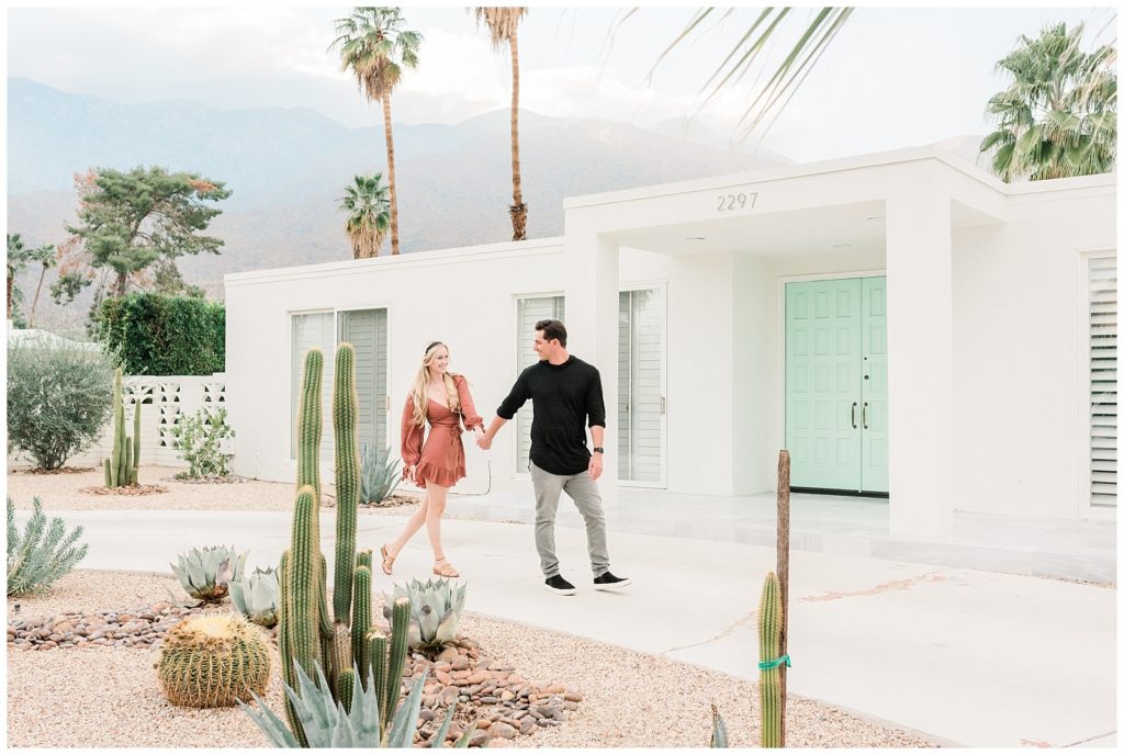 A couple walks  by the teal door during their Palm Springs, California engagement session.