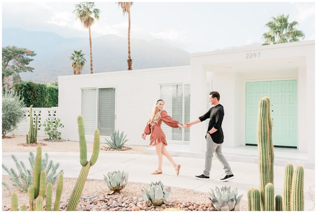 A couple holds hands walking past an iconic home in Palm Springs California for their engagement session.