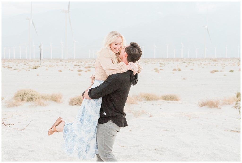 A man lifts and spins his fiancee  during engagement photos in a windmill field in Palm Springs, California.