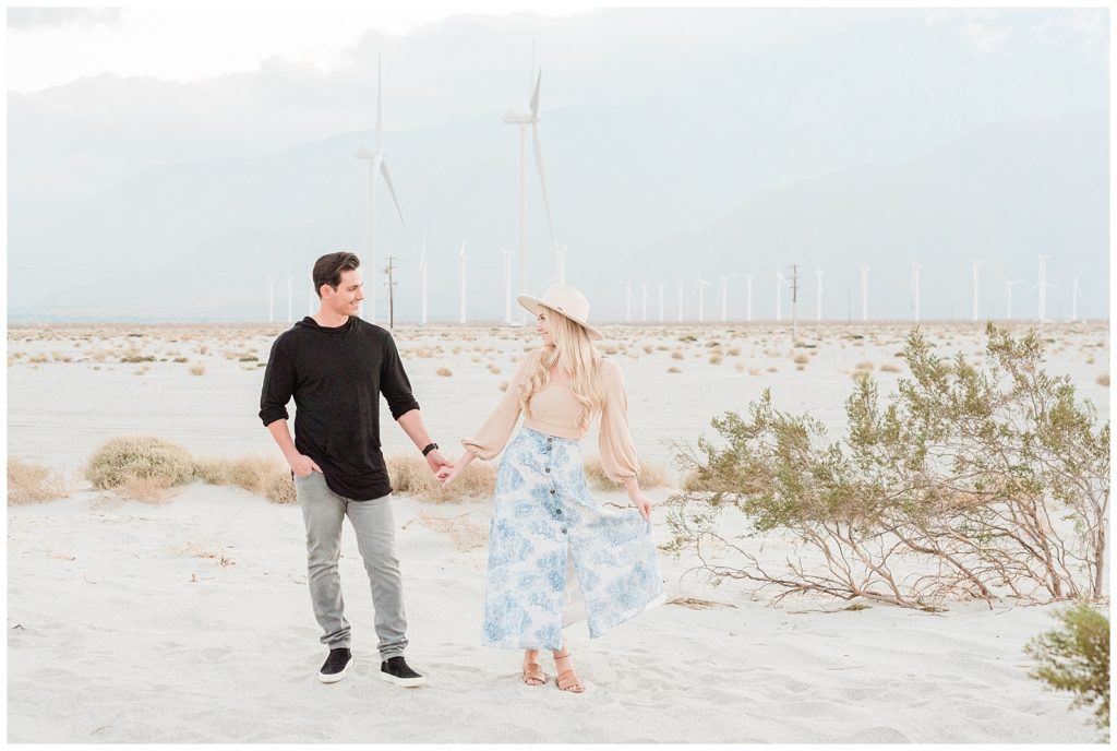 A couple holds hands looking at each other in a Palm Springs windmill field in Southern California.